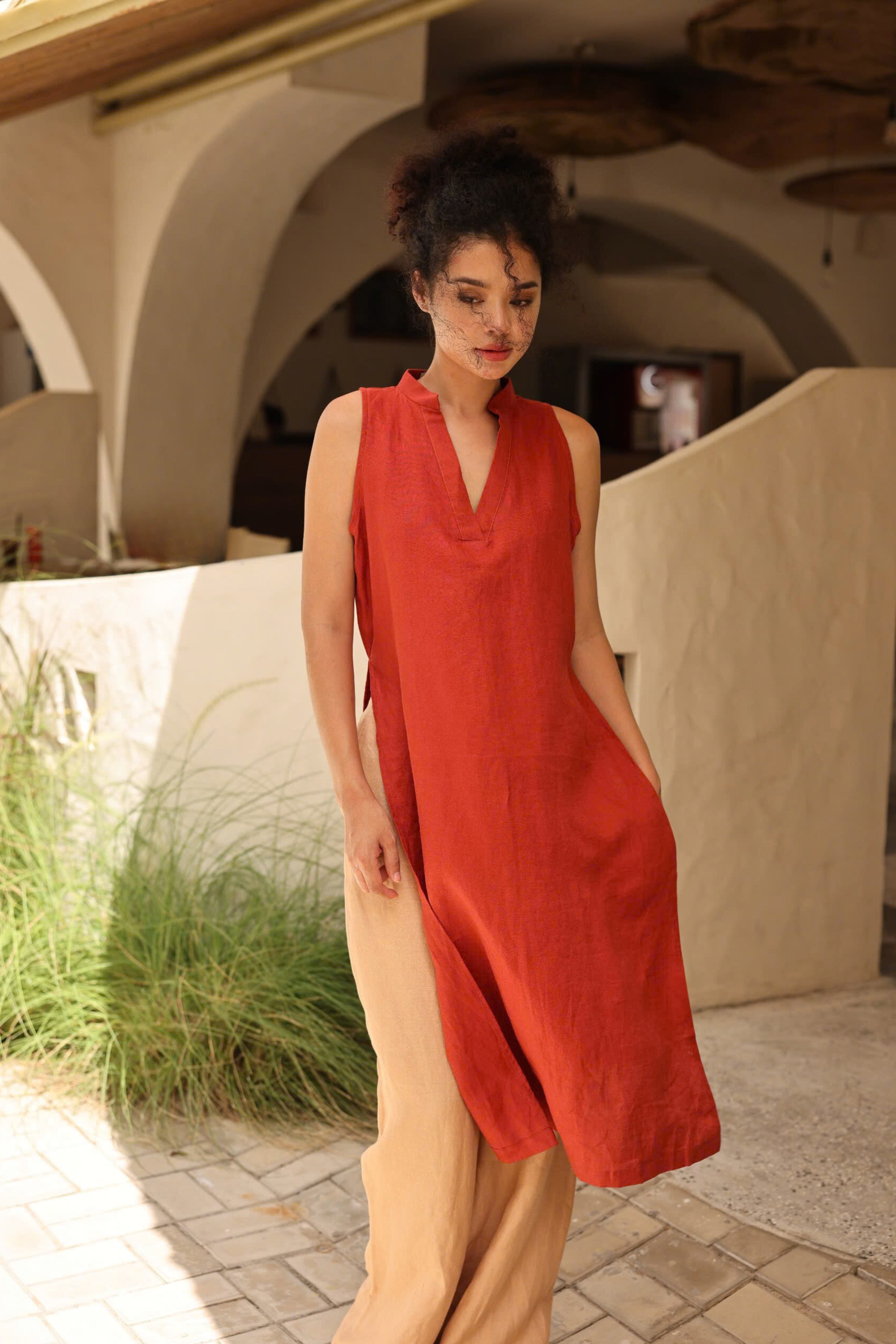 Woman in a red dress standing in an outdoor setting with arches and plants.