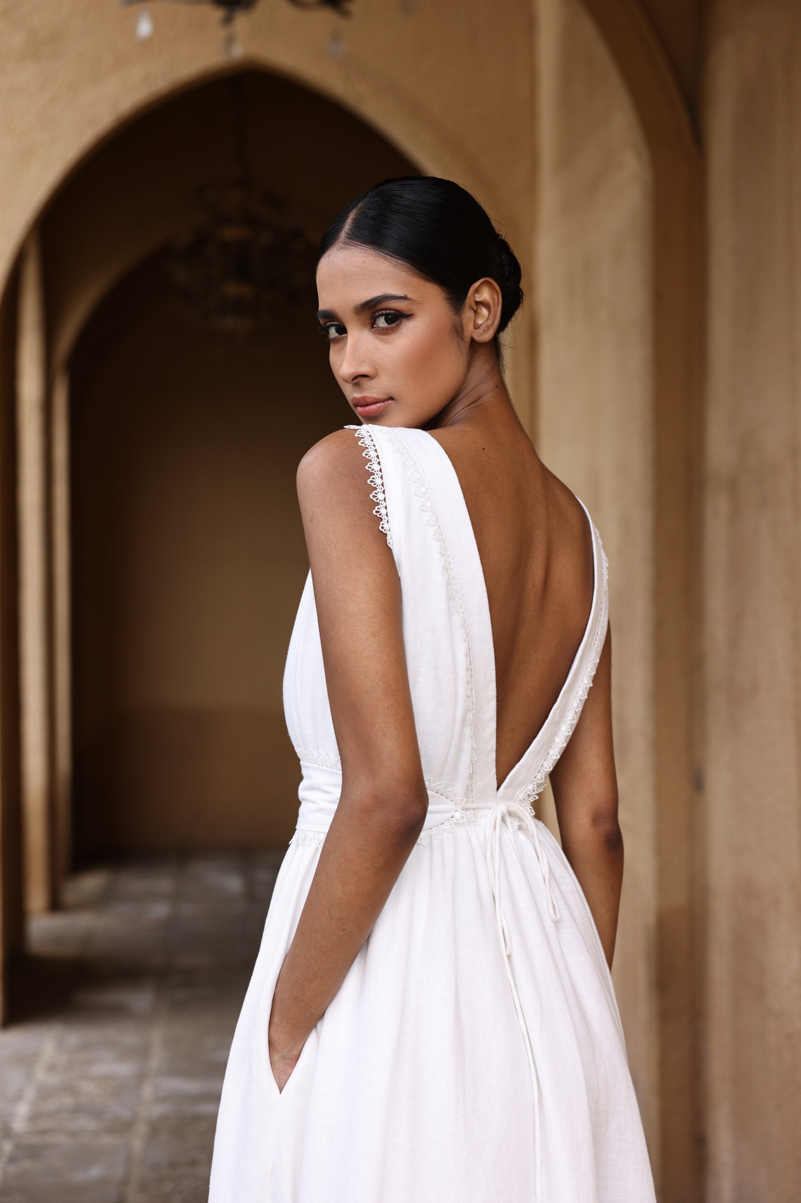 Woman in a white dress with an open back standing in front of a stone archway.