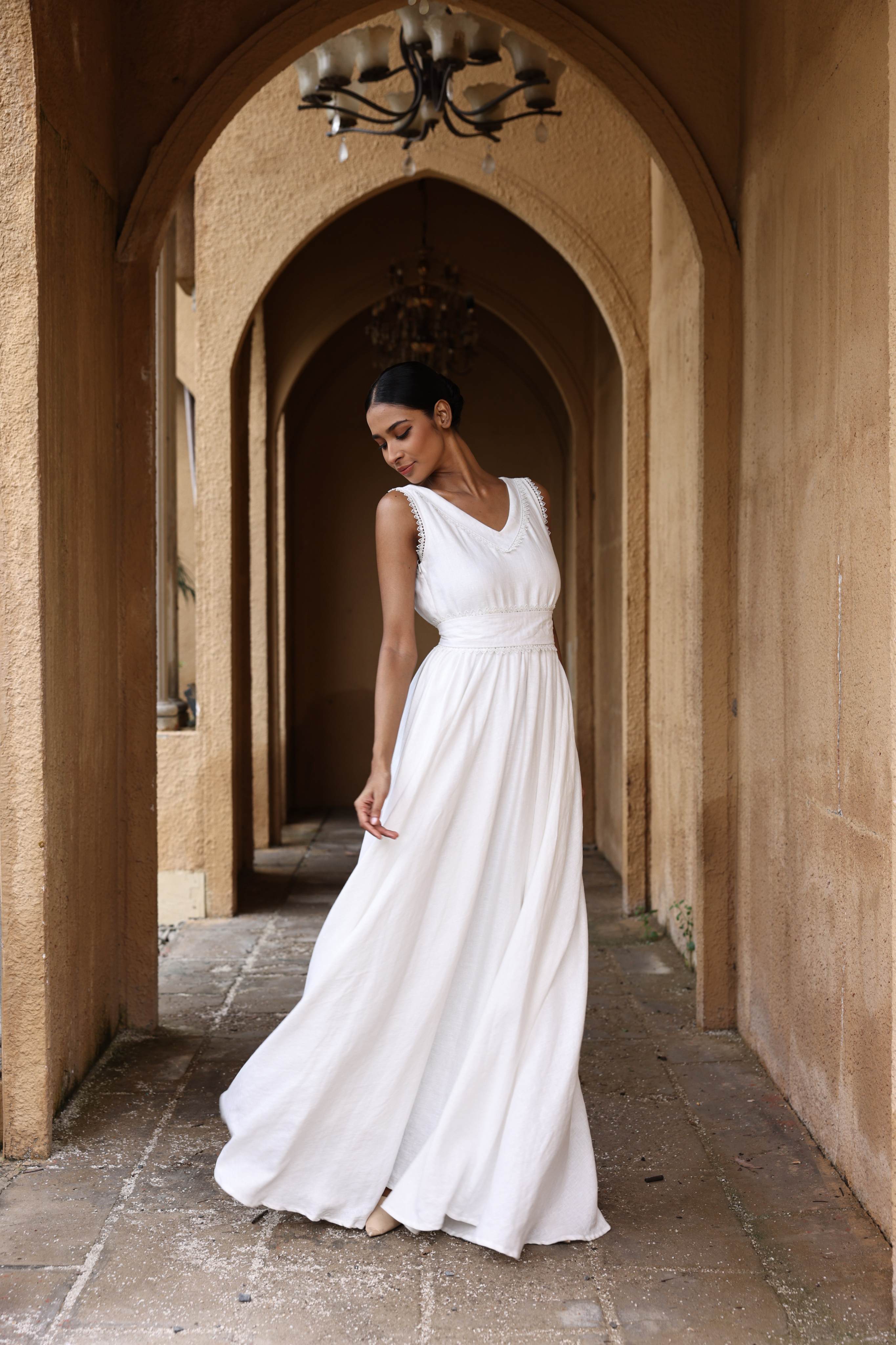 Woman in a white dress standing in an arched stone corridor.