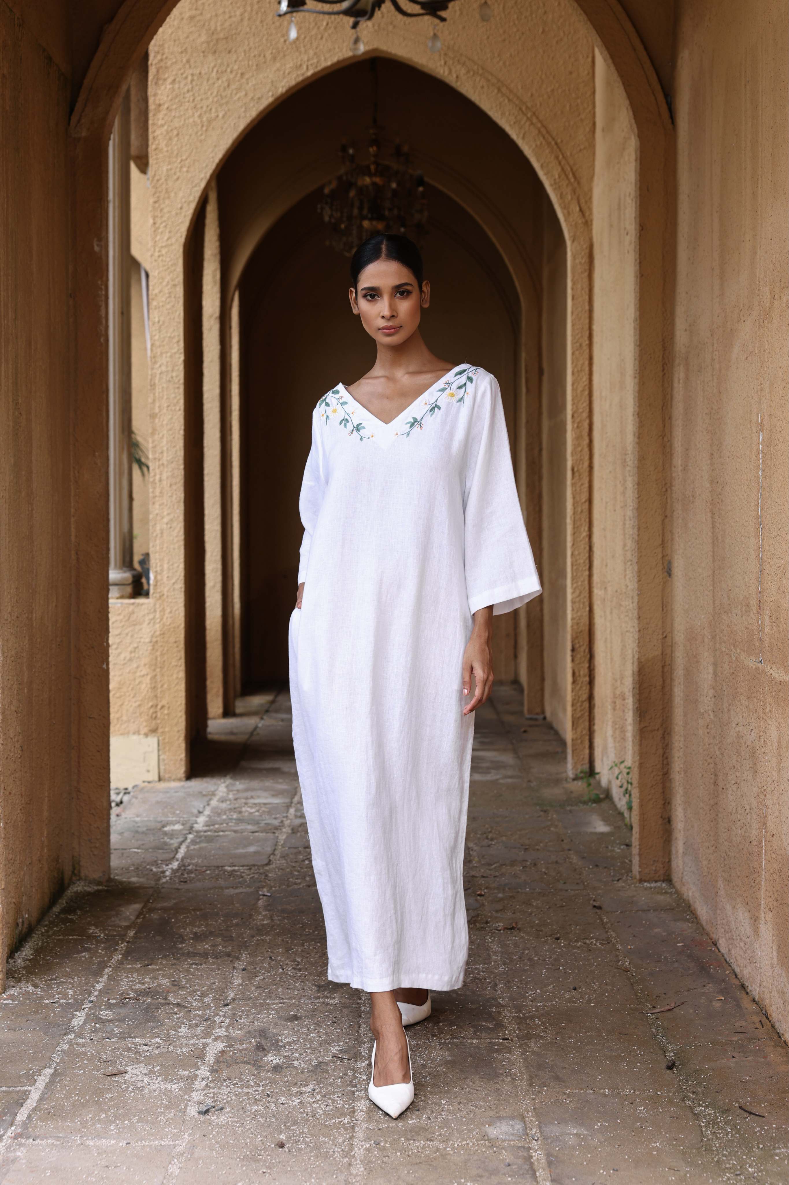 Woman in a white dress standing in an arched stone corridor