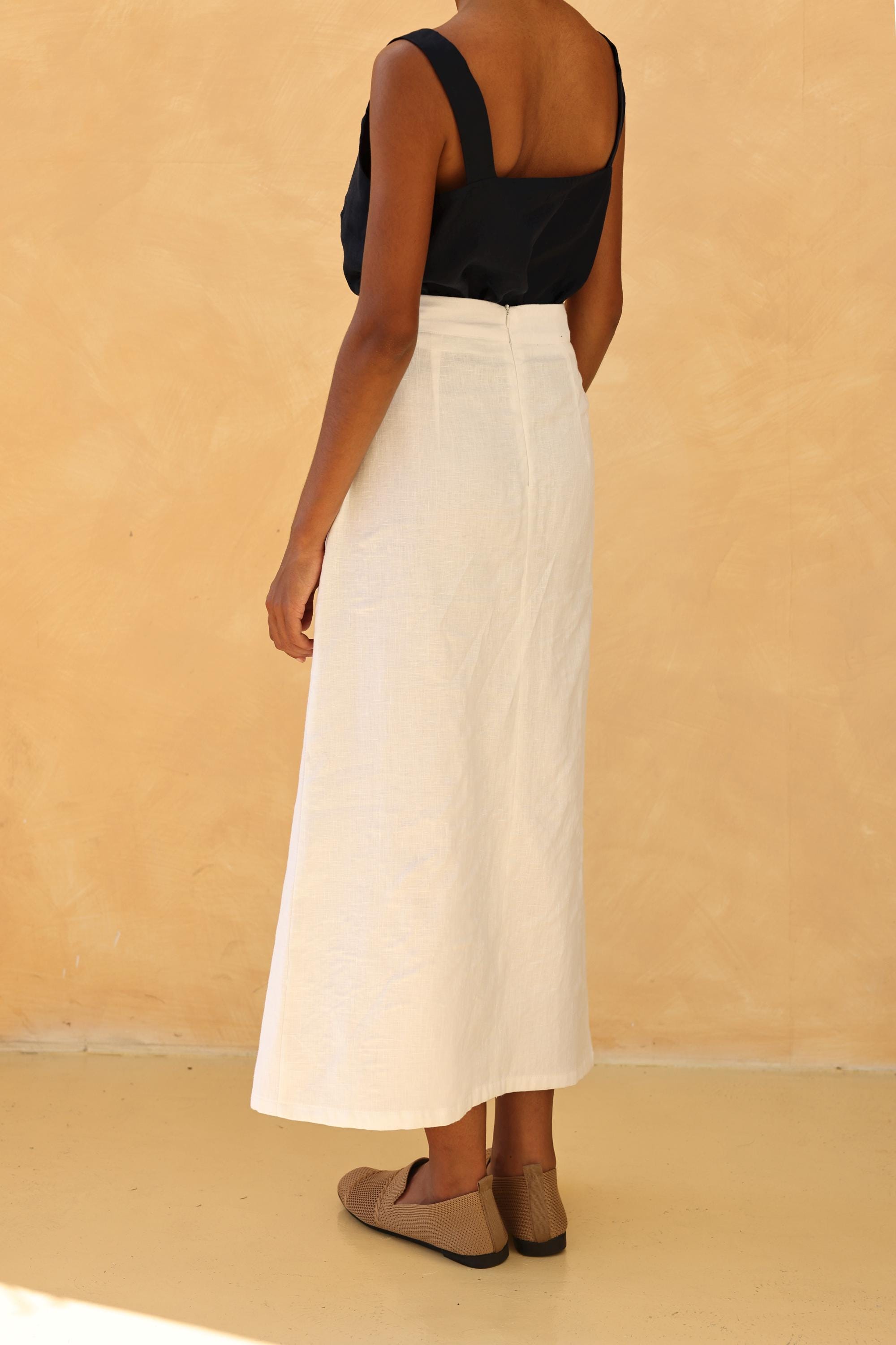 Person wearing a black top and white skirt against a beige background