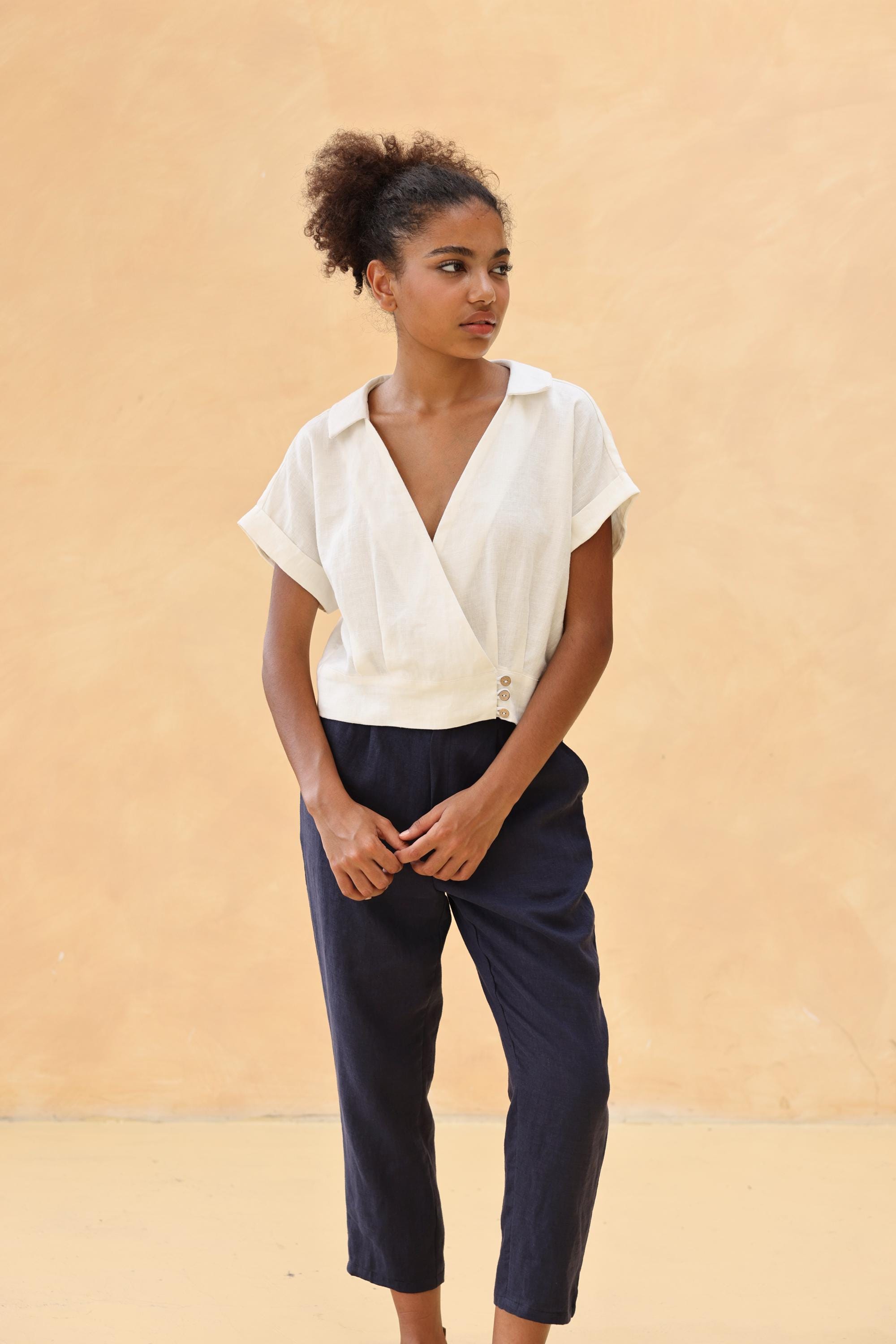 Woman wearing a white blouse and navy pants against a beige background