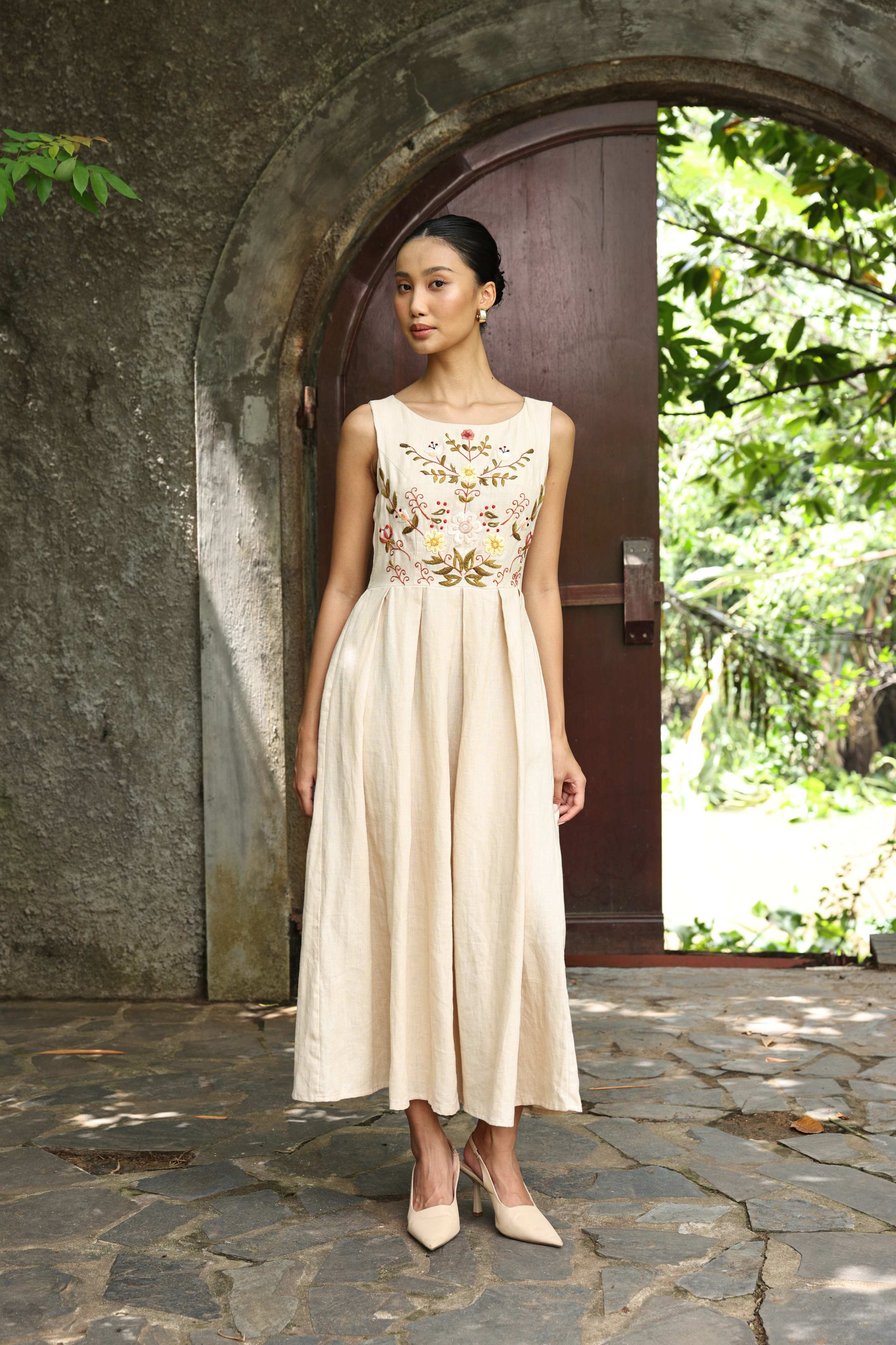 Woman in a dress with floral embroidery standing in front of a stone archway.