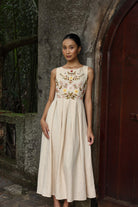 Woman wearing a floral embroidered dress standing against a stone wall.