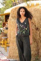 Woman wearing a floral sleeveless top and dark pants standing in front of hay bales.