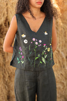 Person wearing a dark sleeveless top with floral embroidery against a blurred natural background