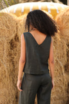 Person wearing a sleeveless top and pants standing in front of hay bales.