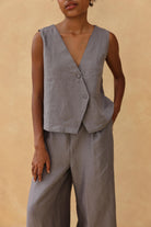 Person wearing a gray vest and pants against a beige background