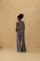 Person wearing a gray sleeveless top and wide-leg pants against a beige wall.