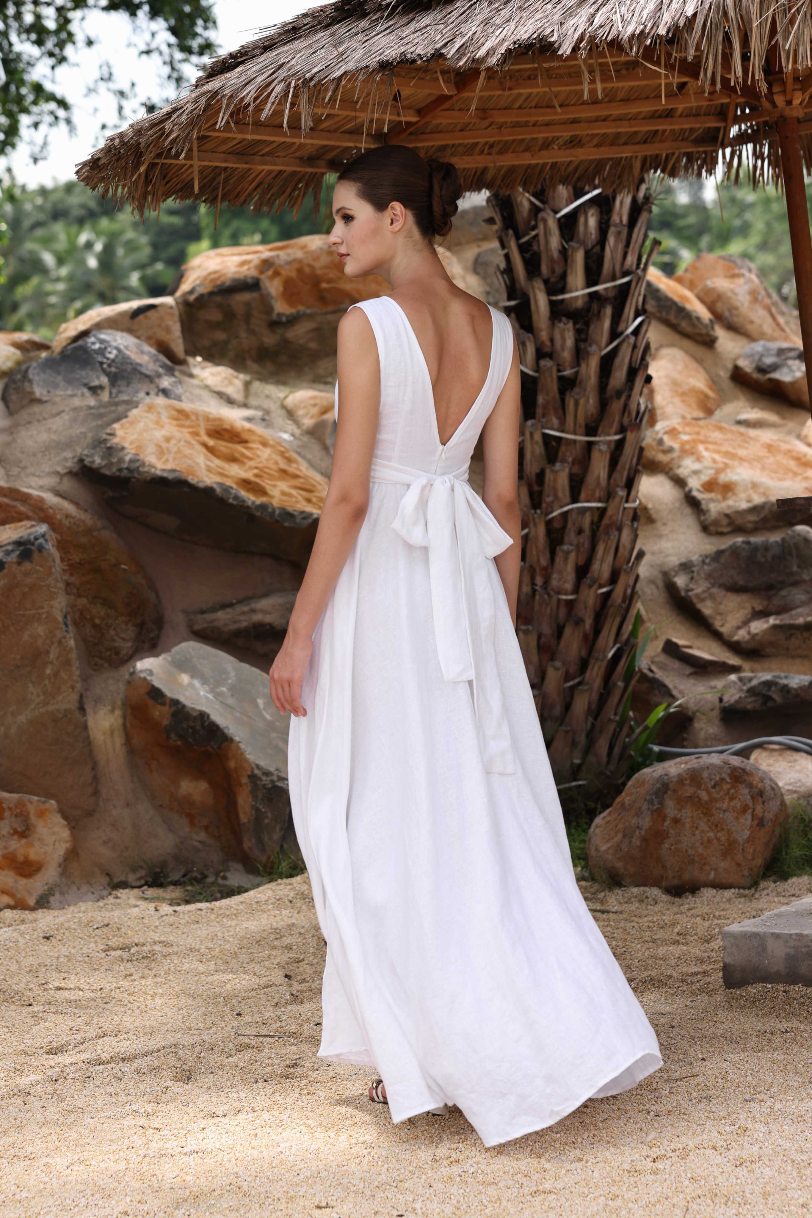 Woman in a white dress standing under a thatched roof with stone walls in the background
