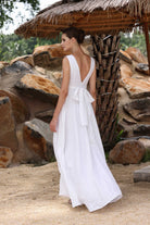 Woman in a white dress standing under a thatched roof with stone walls in the background