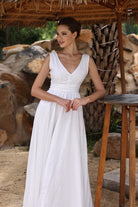 Woman in a white dress standing under a thatched roof with a natural stone background