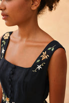 Black sleeveless dress with floral embroidery on a beige background