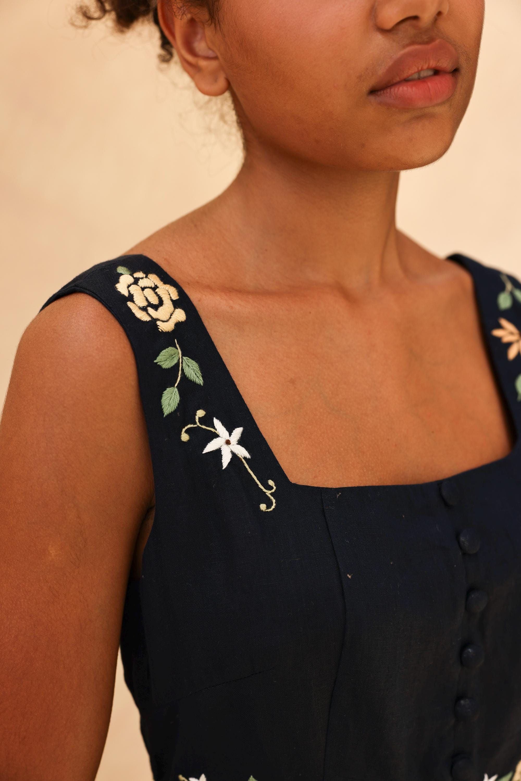 Close-up of a person wearing a black sleeveless dress with floral embroidery on a beige background