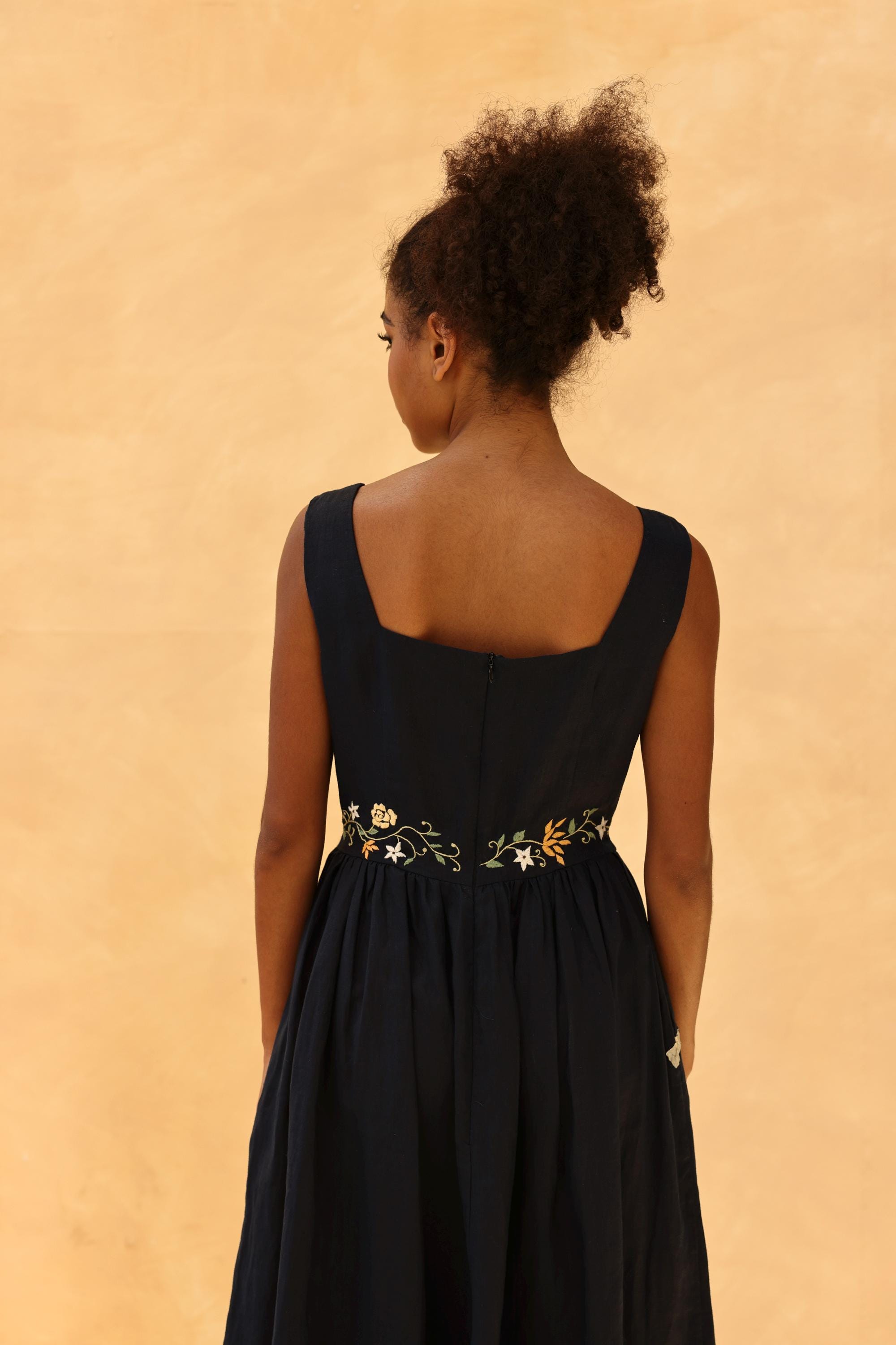 Woman wearing a black dress with floral embroidery on a beige background