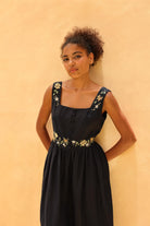 Woman wearing a black dress with floral embroidery against a beige background