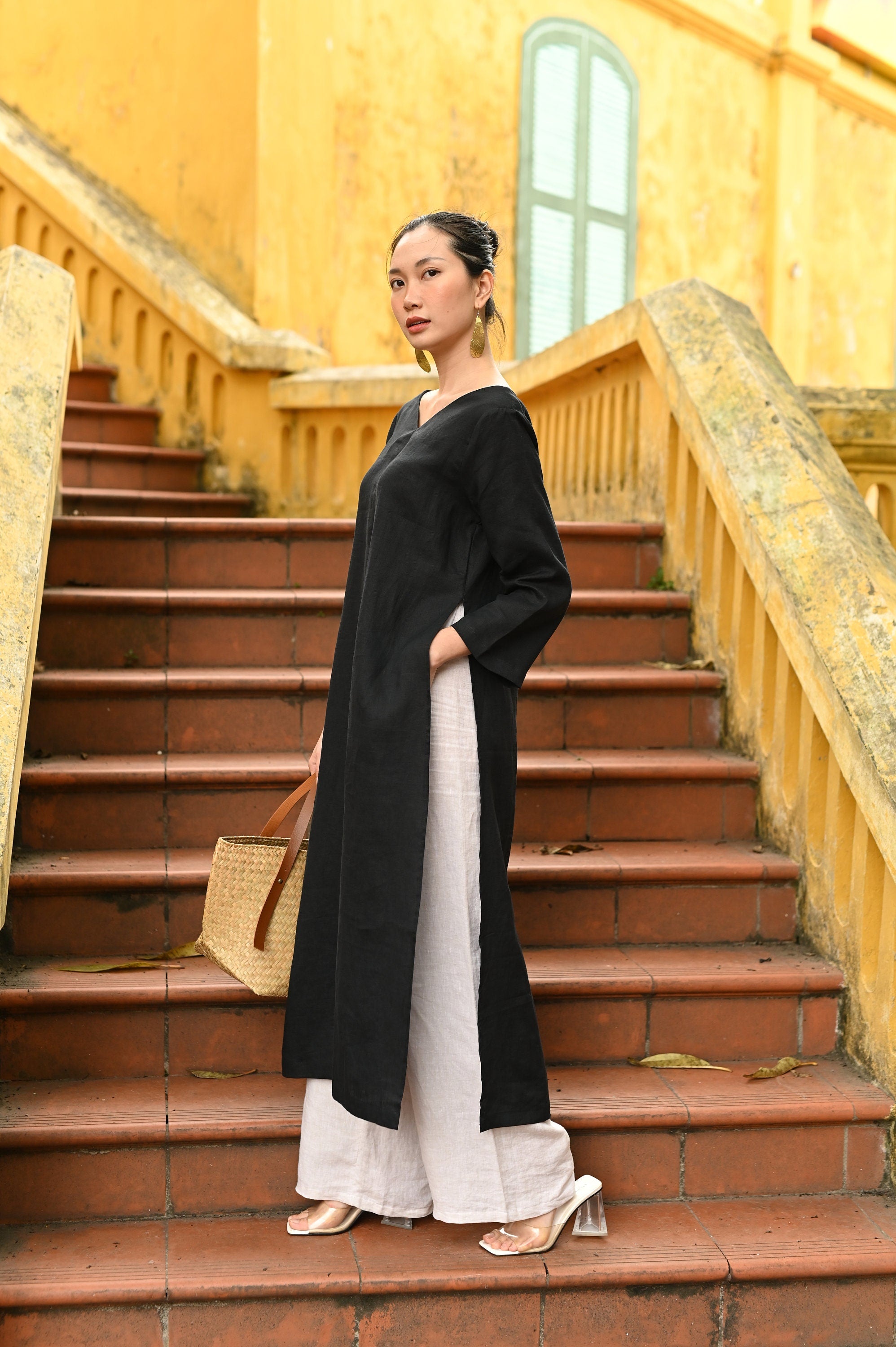Woman in a black and white outfit standing on a yellow building's staircase.