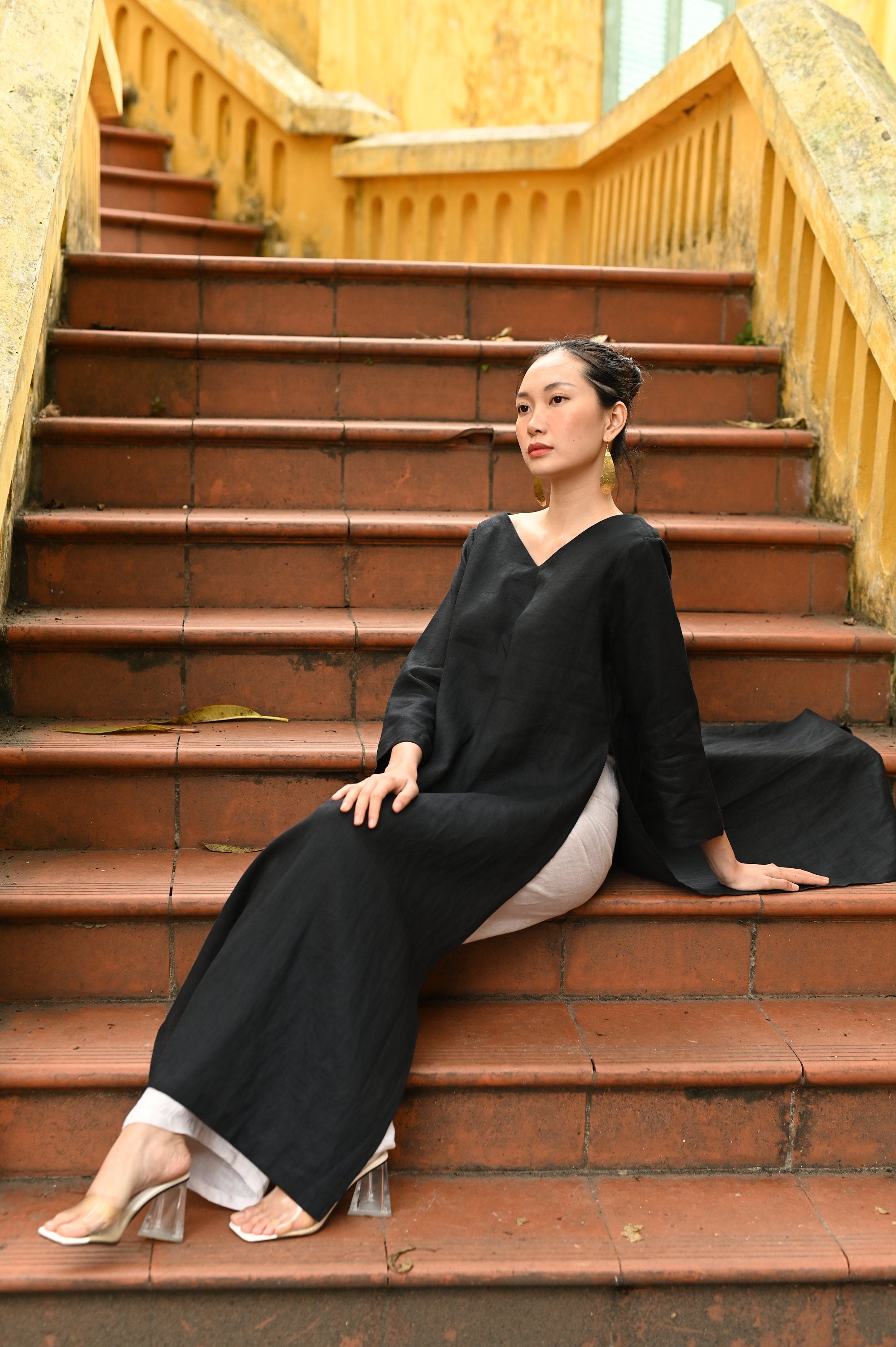 Woman in a black dress sitting on red steps with yellow walls in the background