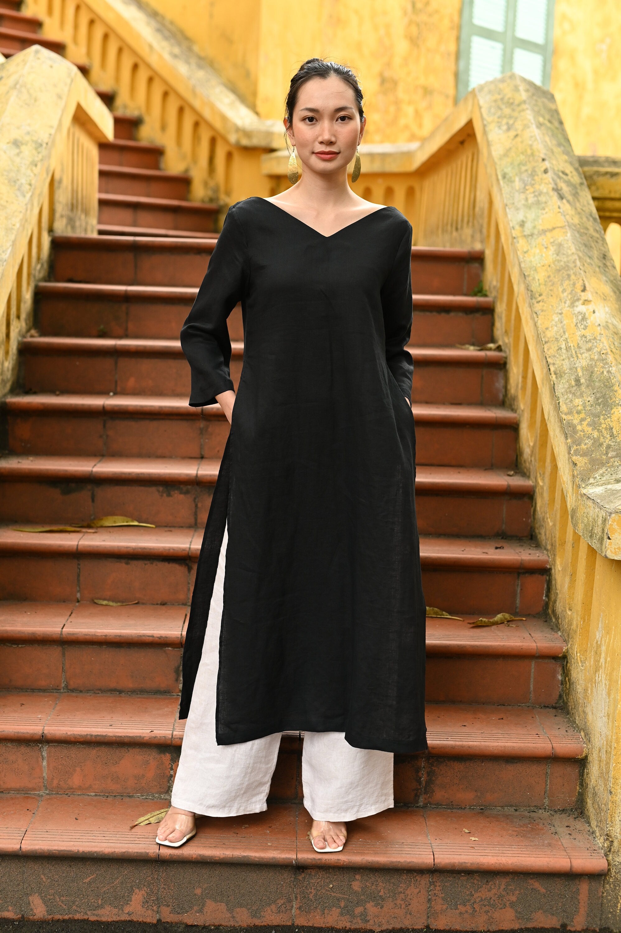 Woman in a black tunic standing on a set of stairs with a yellow wall in the background