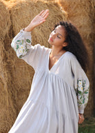 Woman in a dress with floral embroidery standing in front of hay bales.