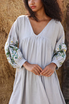 Woman wearing a light gray dress with floral embroidery against a natural background