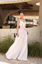 Woman in a white floral dress standing outdoors with plants and a building in the background