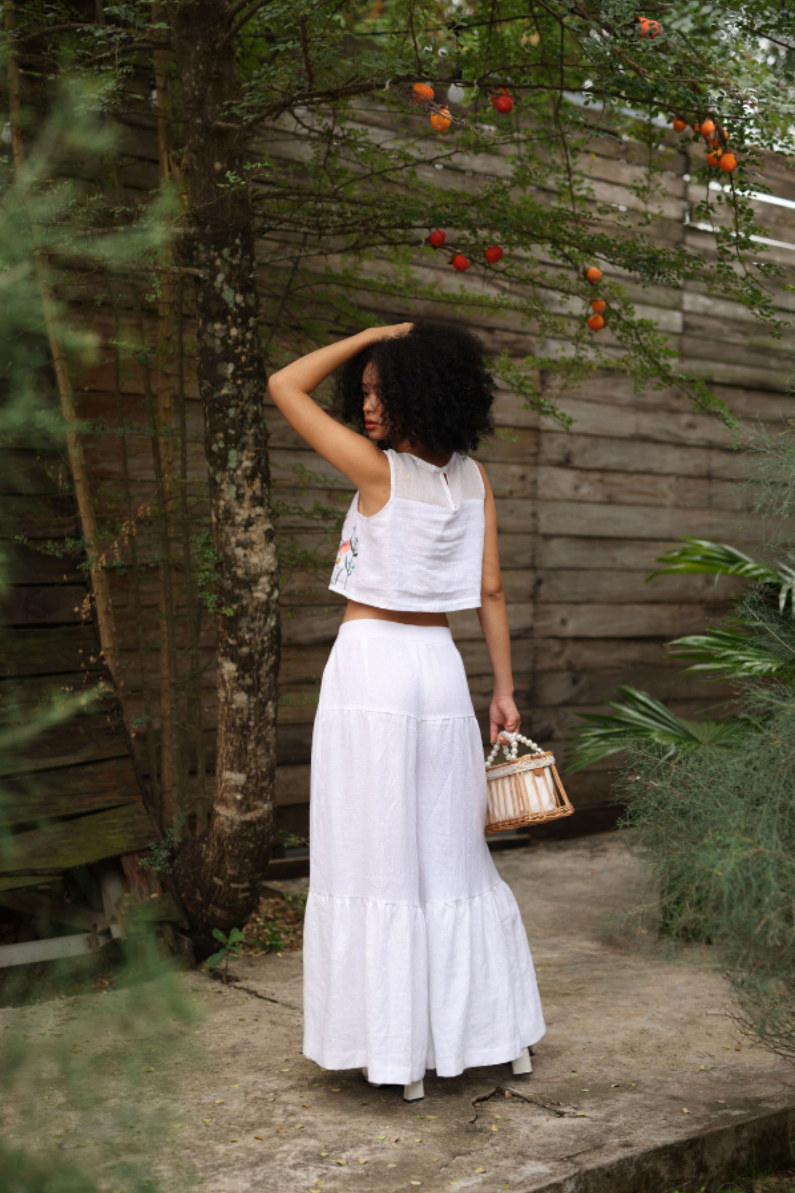 Woman in a white outfit standing in a garden with a wooden fence and plants.