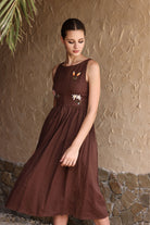 Woman wearing a brown dress with floral details against a textured wall.