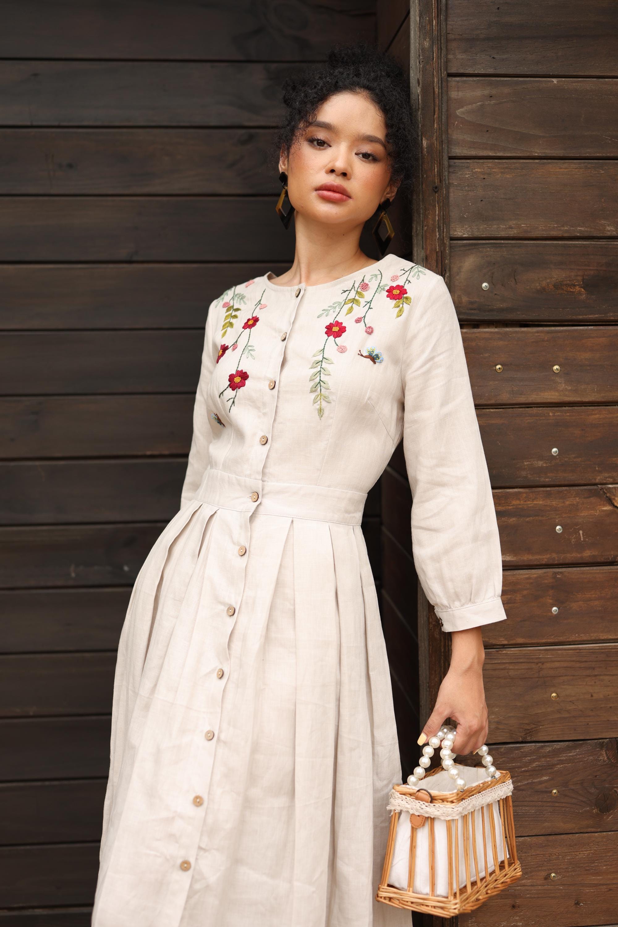 Woman wearing a hand-embroidered dress holding a small bag against a wooden background