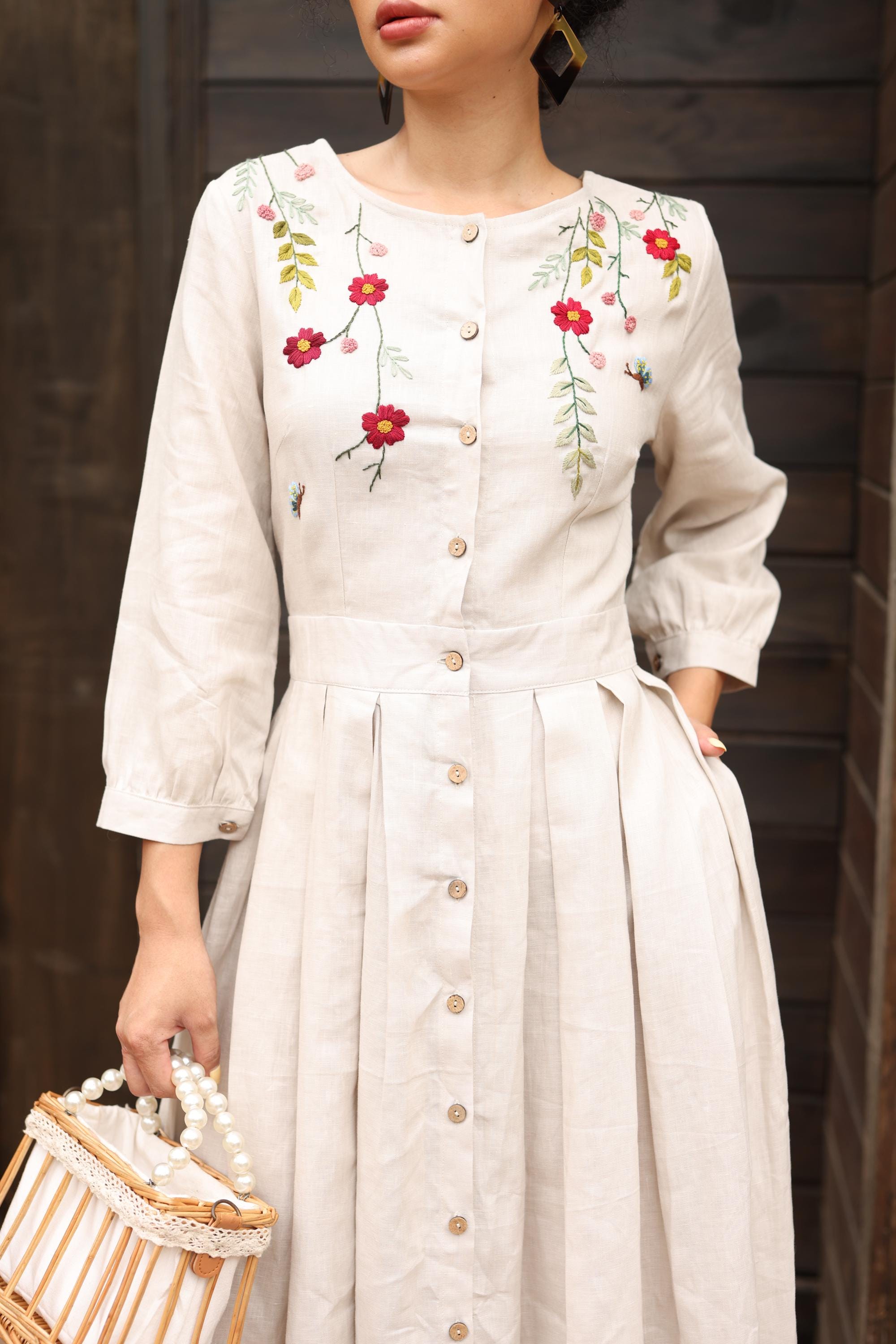 Woman wearing a dress with floral embroidery against a dark wooden background
