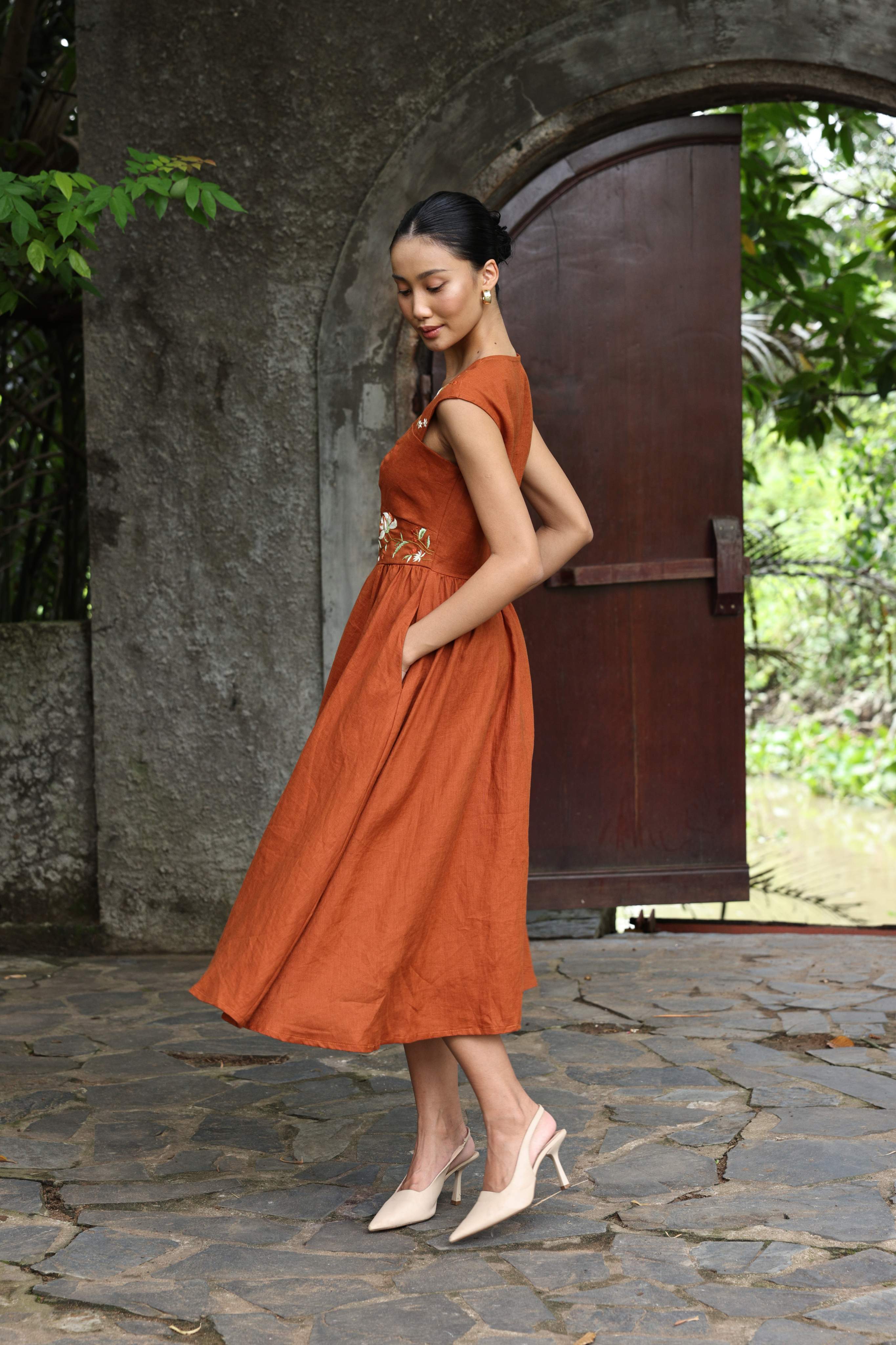 Woman in an orange dress standing in front of a stone archway with greenery.