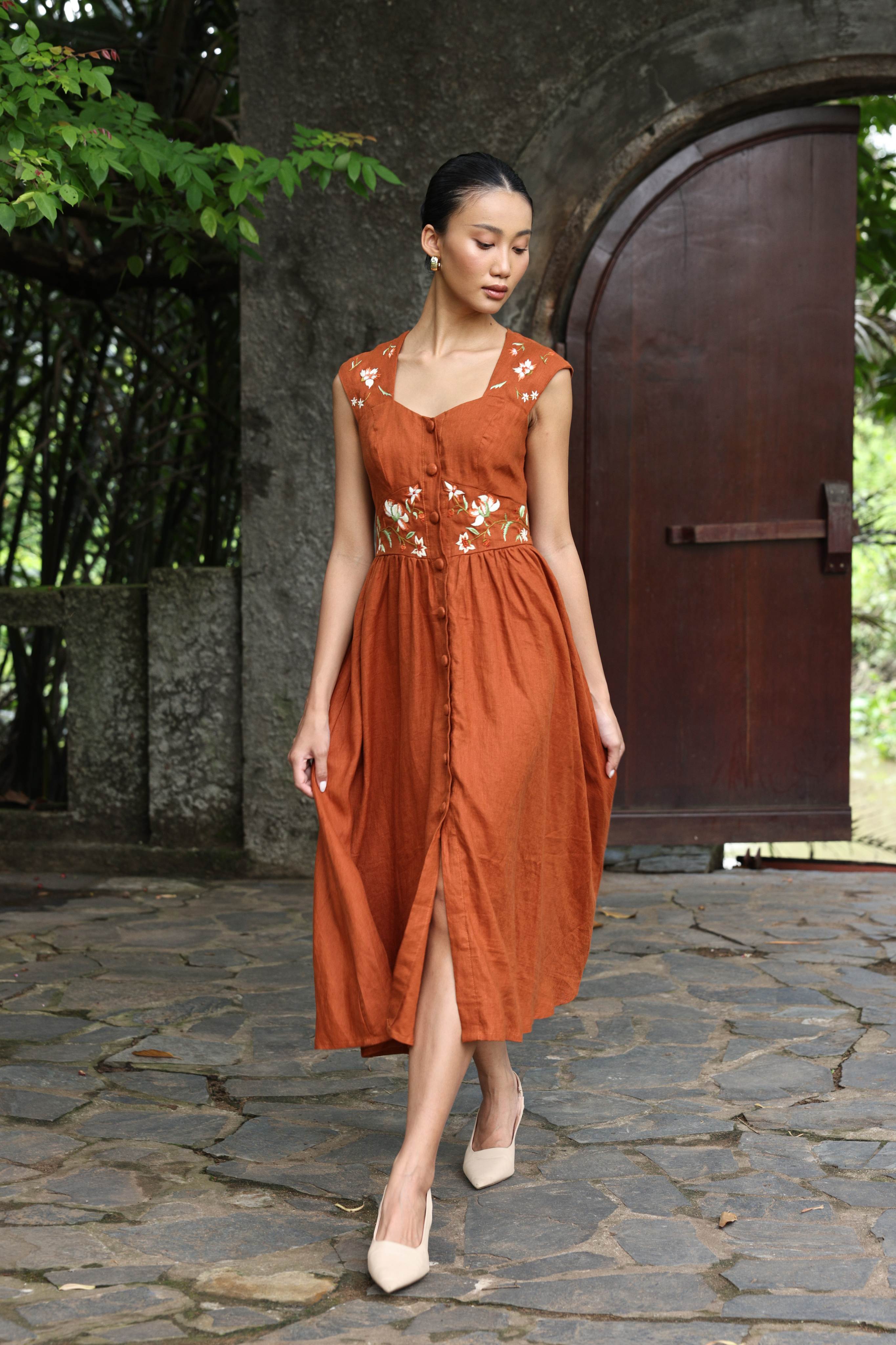 Woman wearing a rust-colored dress with floral patterns in an outdoor setting.