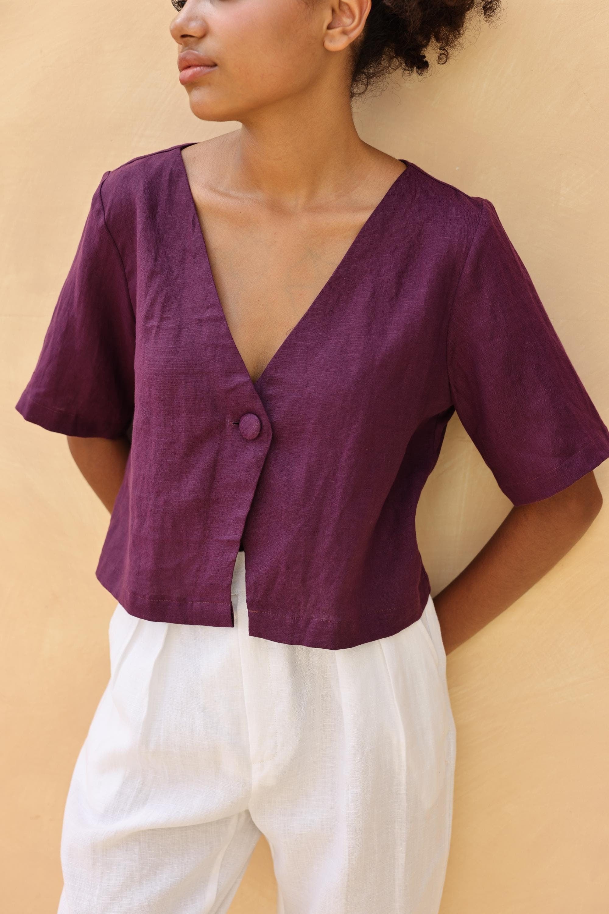 Person wearing a purple top and white pants against a beige background