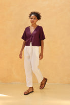 Woman wearing a top and white pants against a beige background