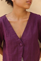 Close-up of a person wearing a purple outfit with a button detail on a beige background