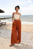 Woman in white top and rust-colored wide-leg pants standing on a beach.