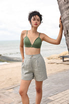 Woman in green bikini top and gray shorts standing on a beach path.