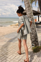 Woman in a gray outfit standing by a palm tree on a beachside path.