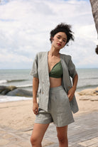Woman in gray blazer and shorts standing on a beach with ocean and sky in the background