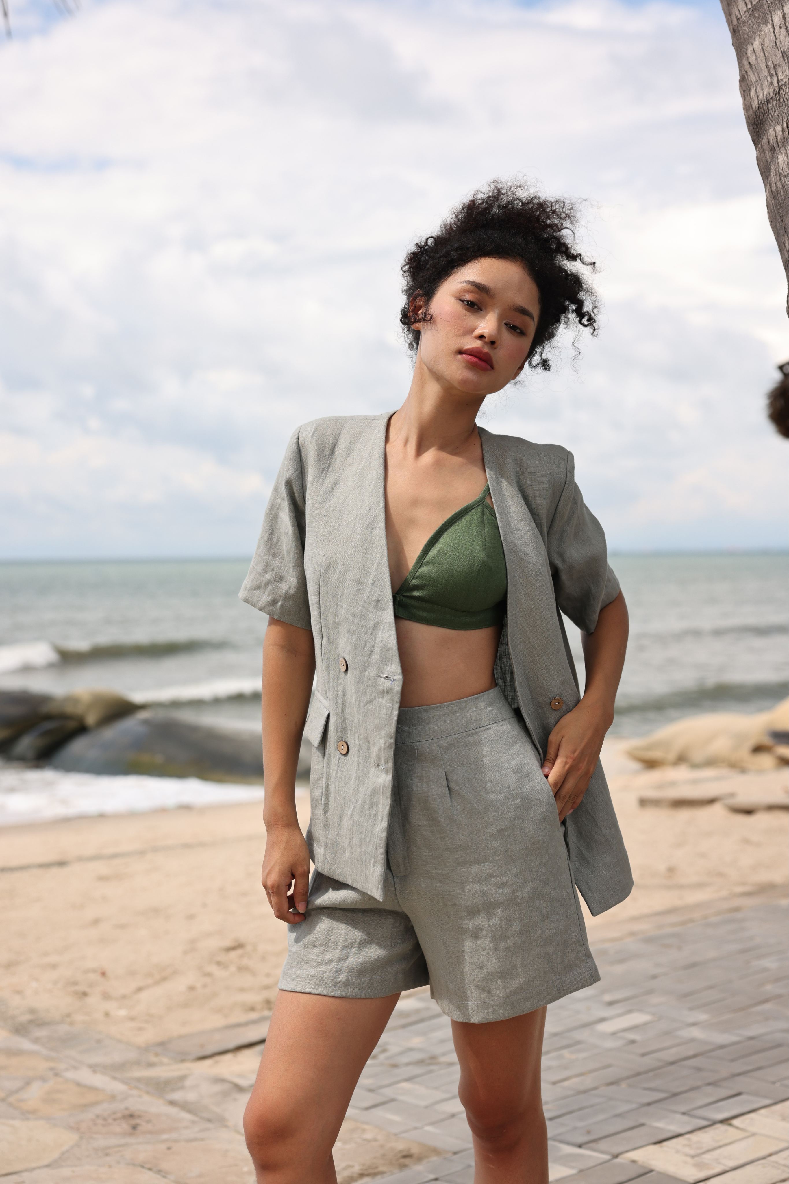 Woman in gray blazer and shorts standing on a beach with ocean and sky in the background