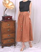 Person wearing a black top and brown buttoned skirt standing next to a wooden dresser with a vintage gramophone.