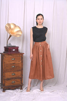 Woman wearing a black top and brown skirt standing next to a vintage wooden record player against a white curtain.