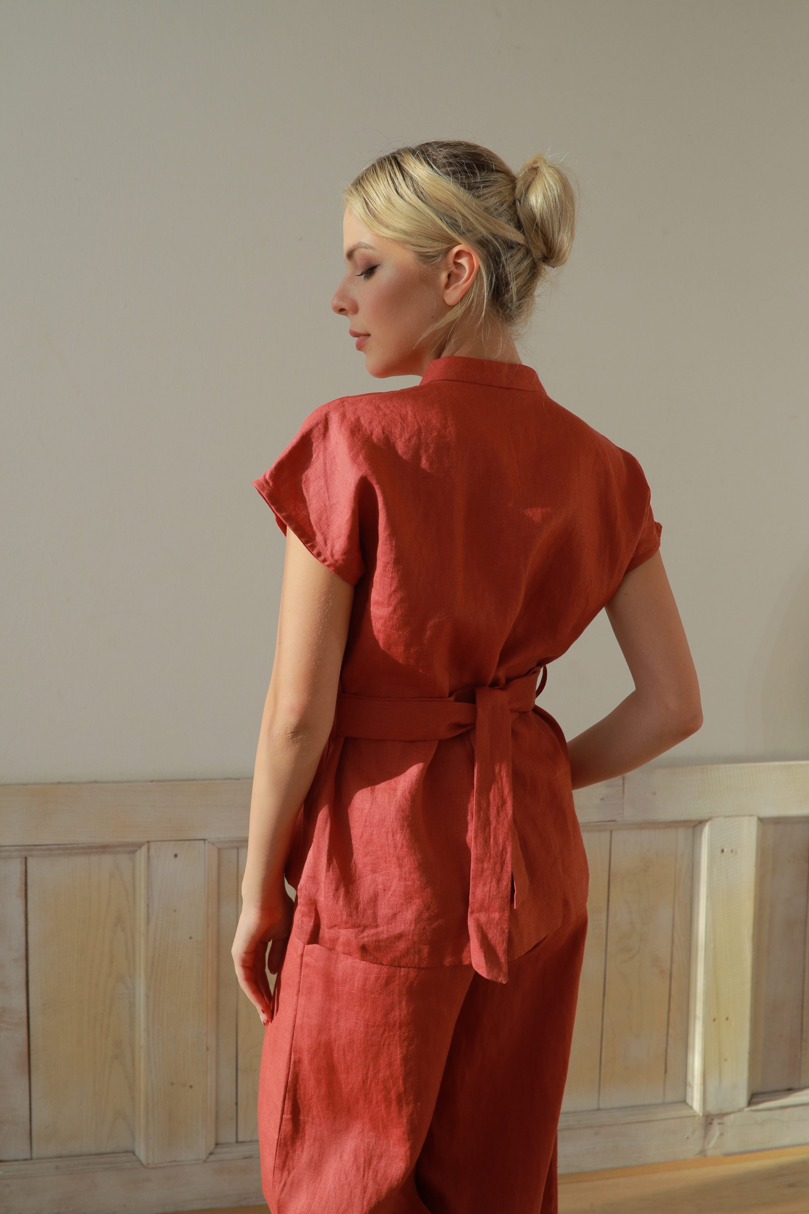 Woman wearing a rust-colored outfit standing against a neutral wall.