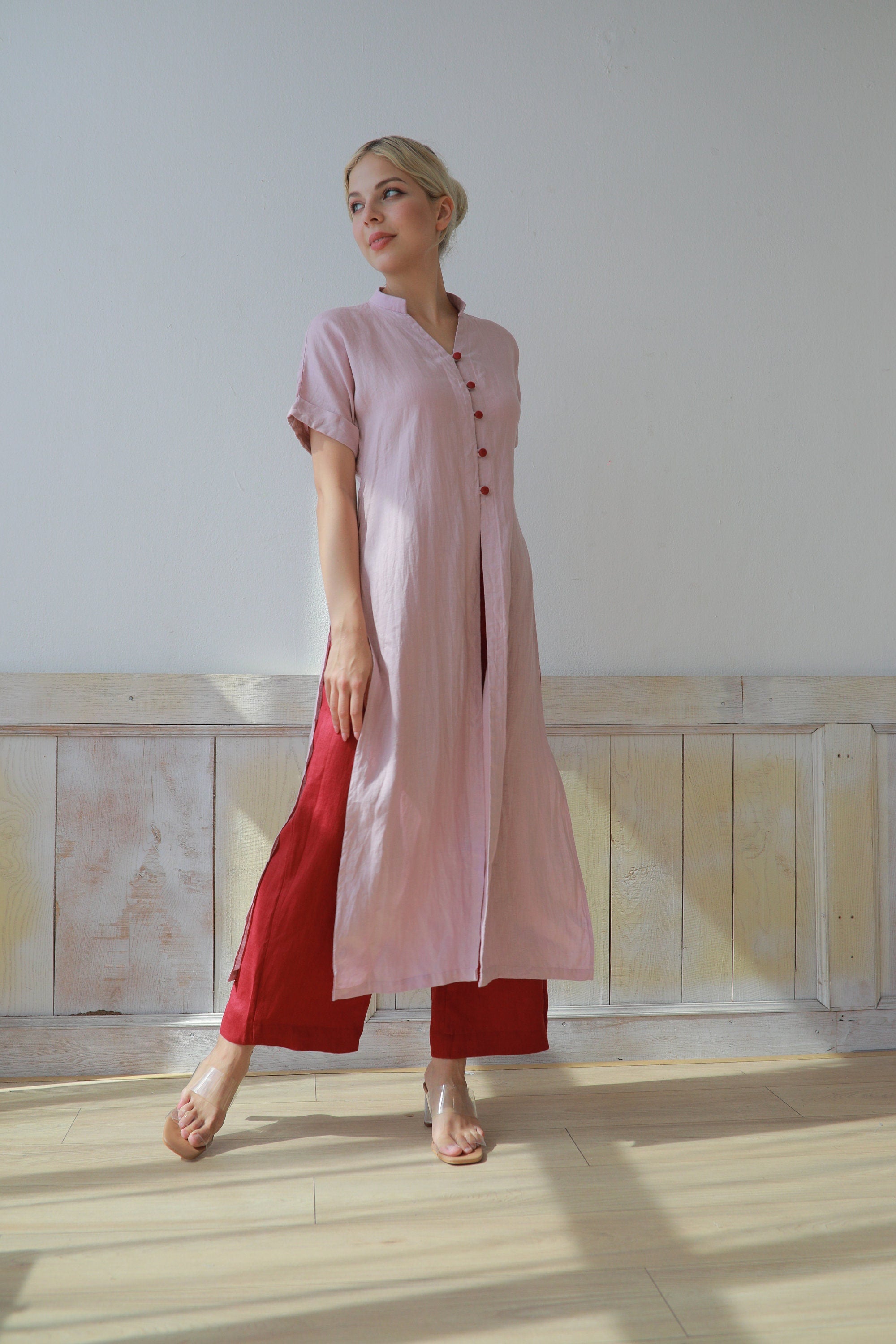 Woman wearing a pink and red outfit standing in a room with light-colored walls and wooden floor.