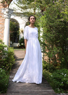 Woman in a white dress standing on a wooden path with greenery around