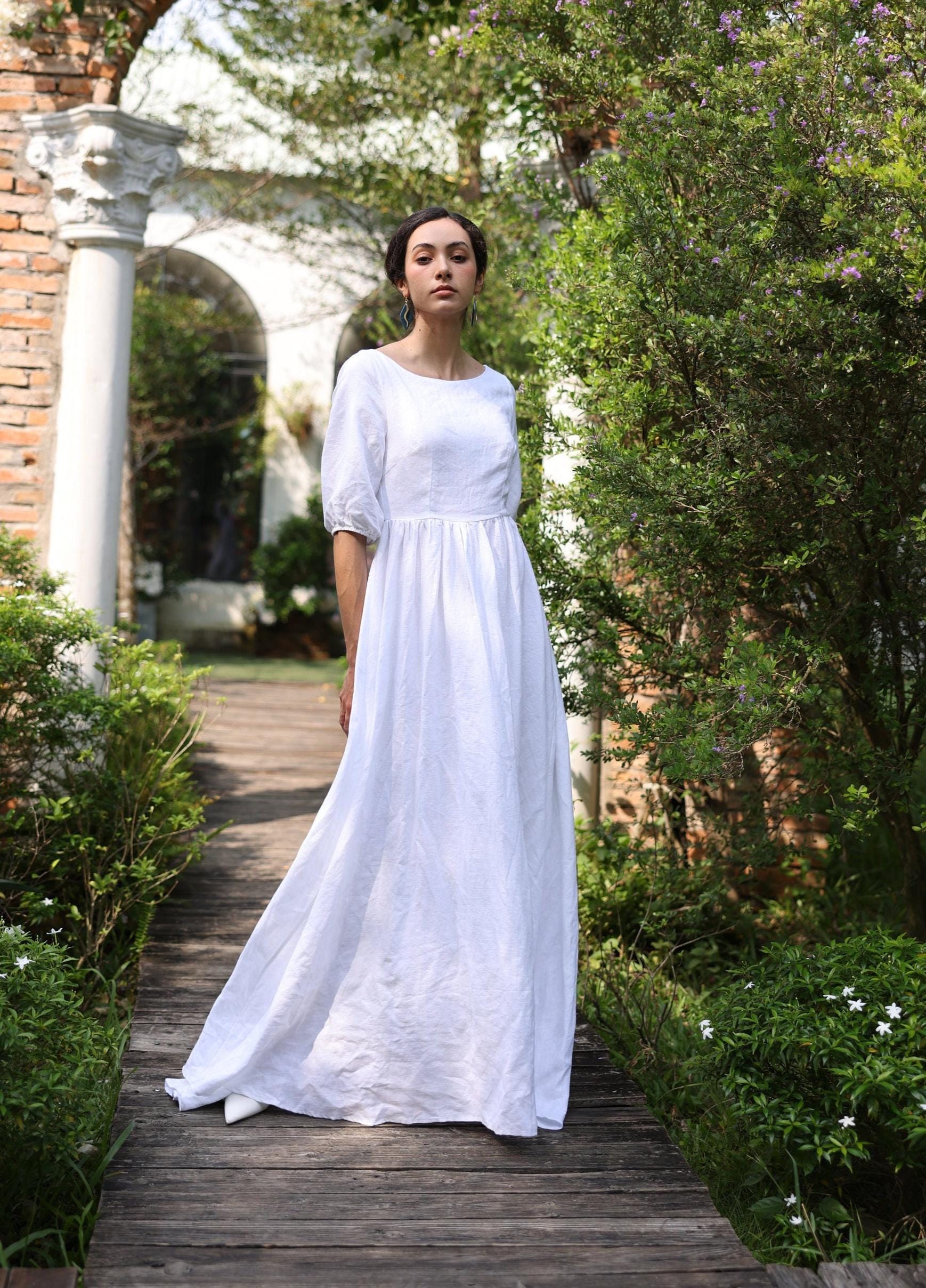 Woman in a white dress standing on a wooden path with greenery around