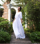 Woman in a white dress standing on a wooden path in a garden setting