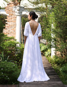 Woman in a white dress standing on a wooden path in a garden.