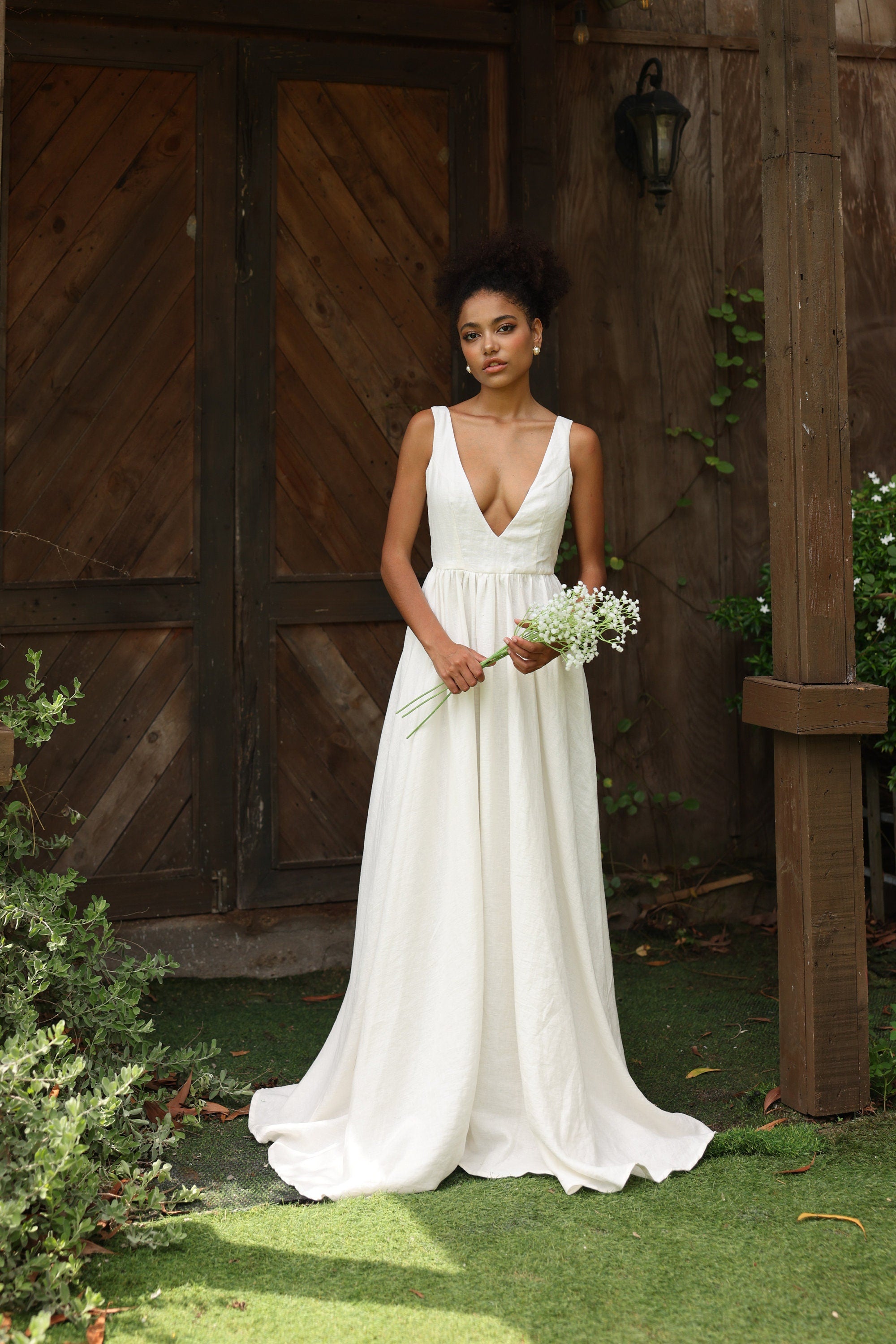 Woman in an ivory wedding dress holding flowers in front of wooden doors.
