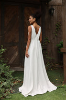 Woman in an ivory dress standing outdoors with a wooden door and greenery in the background